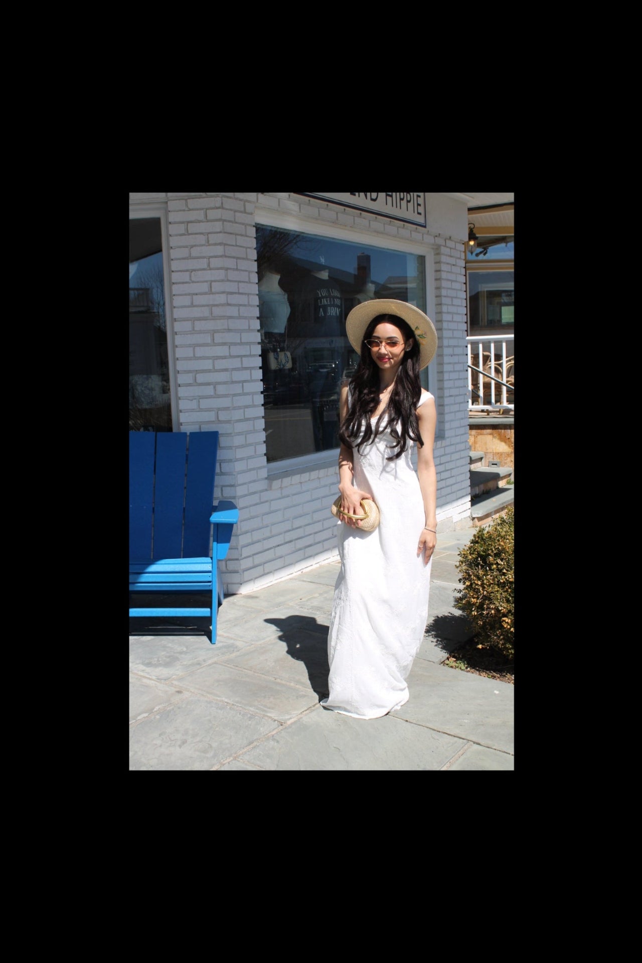 Woman in a white dress and hat standing in front of a building with reflective glass.